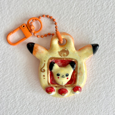 Ceramic keychain sculpture of a Pikachu themed tamagotchi, with an orange keychain and buttons that are like pokeballs.