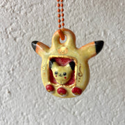 Ceramic keychain sculpture of a Pikachu themed tamagotchi, with an orange keychain and buttons that are like pokeballs.
