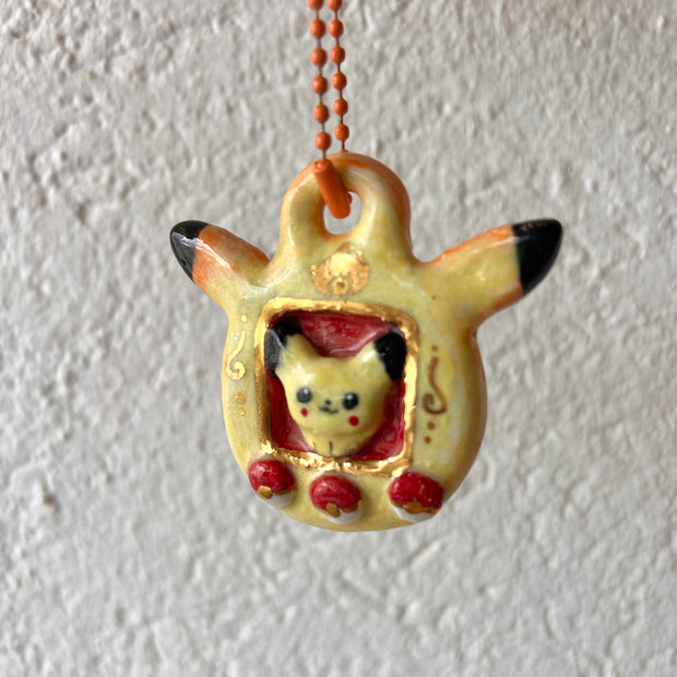 Ceramic keychain sculpture of a Pikachu themed tamagotchi, with an orange keychain and buttons that are like pokeballs.