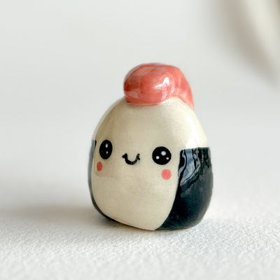 Ceramic sculpture shaped like a piece of sushi or onigiri with a smiling face on a white background