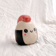 Ceramic sculpture shaped like a piece of sushi or onigiri with a smiling face on a white background