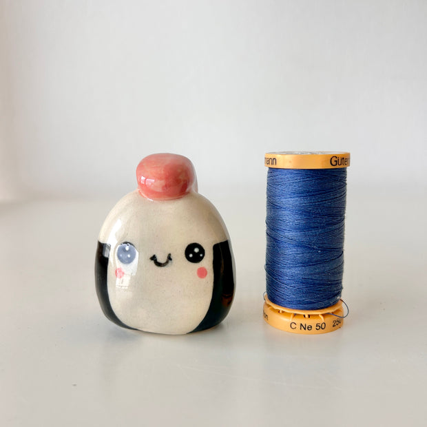 Ceramic sculpture shaped like a piece of sushi or onigiri with a smiling face on a white background