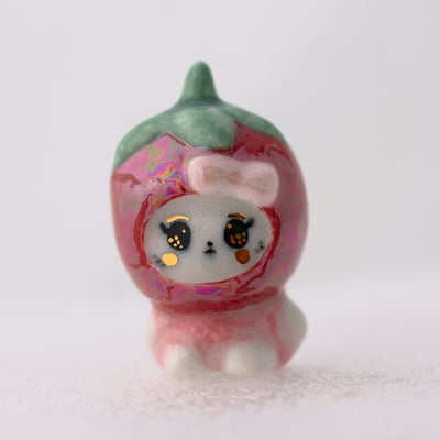 Small figurine of a cat in a pink dress with a bow on a white background
