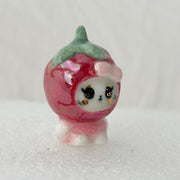 Small figurine with a pink body and green top on a white background