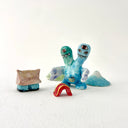 Small collection of sculptures: a house, a tiny red bridge, mountains and a 2-headed blue water monster.