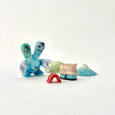 Small collection of sculptures: a house, a tiny red bridge, mountains and a 2-headed blue water monster.