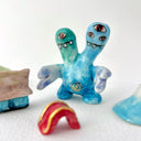 Small collection of sculptures: a house, a tiny red bridge, mountains and a 2-headed blue water monster.