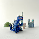 Small collection of sculptures: several buildings, a cherry blossom tree, green hill and a blue kaiju monster with gold dots.