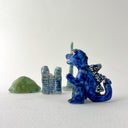 Small collection of sculptures: several buildings, a cherry blossom tree, green hill and a blue kaiju monster with gold dots.