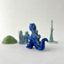Small collection of sculptures: several buildings, a cherry blossom tree, green hill and a blue kaiju monster with gold dots.