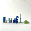 Small collection of sculptures: several buildings, a cherry blossom tree, green hill and a blue kaiju monster with gold dots.
