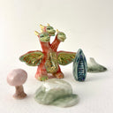 Small collection of sculptures: a three-headed monster, a small cherry blossom tree, green mountain and other nature elements.