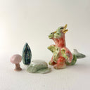 Small collection of sculptures: a three-headed monster, a small cherry blossom tree, green mountain and other nature elements.