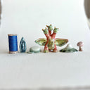 Small collection of sculptures: a three-headed monster, a small cherry blossom tree, green mountain and other nature elements.