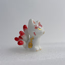 White ceramic cat figurine, sitting with 9 tails that are red-tipped. The cat's face and body has gold painted detailings.