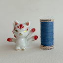 White ceramic cat figurine, sitting with 9 tails that are red-tipped. The cat's face and body has gold painted detailings.