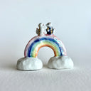 Small ceramic sculpture of a rainbow with clouds on the ends and 2 tiny foxes standing at the top, facing each other as though they are getting married.