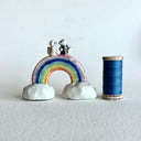 Small ceramic sculpture of a rainbow with clouds on the ends and 2 tiny foxes standing at the top, facing each other as though they are getting married.