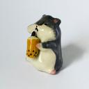 Ceramic sculpture of a gray and white hamster, sitting and holding a cup of thai tea boba.
