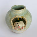 Glazed ceramic pot with a small puppy breaking out of the center, dressed up in a green kaiju costume with a menacing expression.