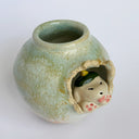 Glazed ceramic pot with a small puppy breaking out of the center, dressed up in a green kaiju costume with a menacing expression.
