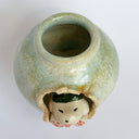 Glazed ceramic pot with a small puppy breaking out of the center, dressed up in a green kaiju costume with a menacing expression.