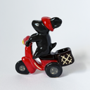 Ceramic sculpture of a black bunny with a red visor, riding a red motorized scooter with a basket on the back.