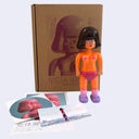 Vinyl toy figure of a topless woman with glittery orange skin and pink underwear.