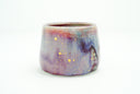 Glossy ceramic cup with a deep reddish purple to light blue gradient coloring with gold sparkles on it. 
