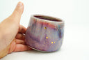 Glossy ceramic cup with a deep reddish purple to light blue gradient coloring with gold sparkles on it. 