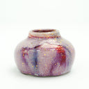 Glossy ceramic vase with a small opening and  a deep reddish purple to light blue gradient coloring with gold sparkles on it. 