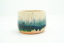 Ceramic cup with a glossy finish and an coloring of light yellow, teal blue and light orange that lightly bleeds into one another like a more abrupt, melty gradient. 