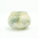 Small ceramic pot with a cream colored and light green glossy exterior with many small divets like the surface of a moon.