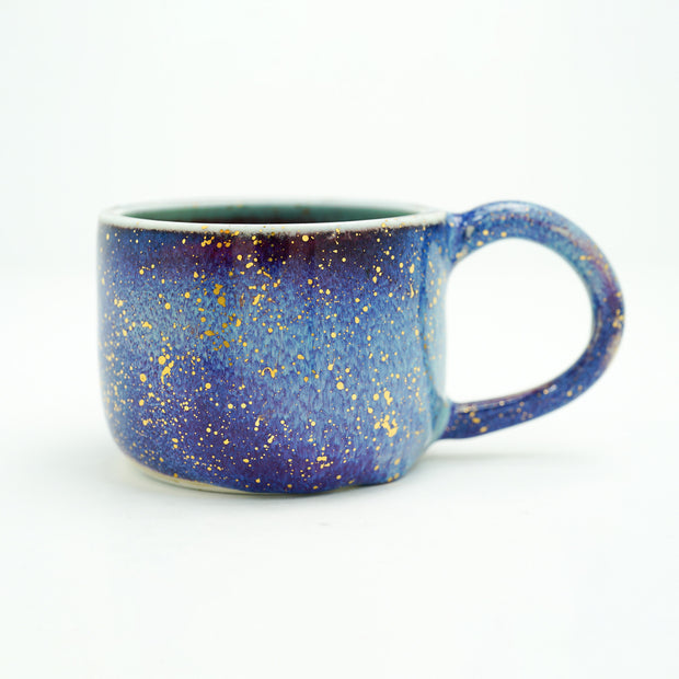 Glossy ceramic handle mug with a dark blue to light blue gradient coloring with gold sparkles on it. 