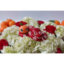 Ceramic sculpture of a red snake with large, cute eyes and white flower patterning atop its body. It has its tongue out and nestled into the snake's body is a small mandarin orange with large eyes.