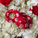 Ceramic sculpture of a red snake with large, cute eyes and white flower patterning atop its body. It has its tongue out and is seen from overhead.