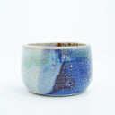 Short ceramic bowl with a blue multicolor glaze and golden splatters.