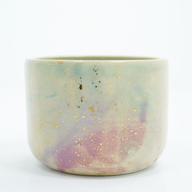 Short ceramic bowl with a light green and light purple multicolor glaze and golden splatters.