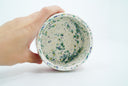 Inside view of ceramic bowl, off white with green and blue splotches and gold speckles.