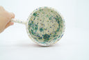 Inside view of ceramic mug, off white with green and blue splotches and gold speckles.