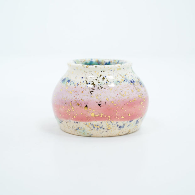 Small ceramic pot, with small opening mostly off white with a light pink stripe running through the middle. Blue and gold speckles decorate the surface.
