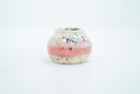 Small ceramic pot, with small opening mostly off white with a light pink stripe running through the middle. Blue and gold speckles decorate the surface.