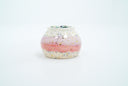 Small ceramic pot, with small opening mostly off white with a light pink stripe running through the middle. Blue and gold speckles decorate the surface.