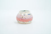 Small ceramic pot, with small opening mostly off white with a light pink stripe running through the middle. Blue and gold speckles decorate the surface.