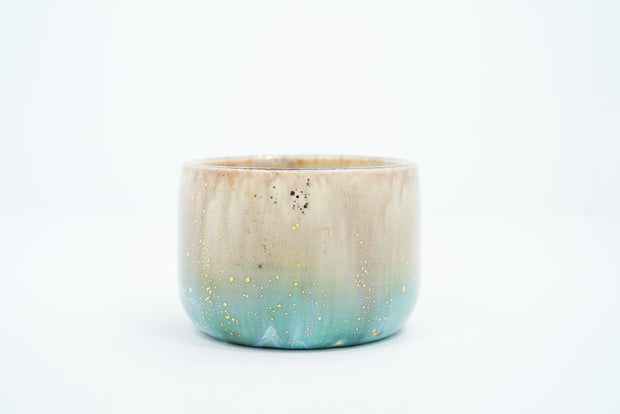 Small ceramic cup with a gradient of light brown to blue and gold speckles.