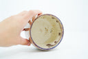 Inside view of ceramic cup, with blue and purple lining the rim and off white inside with gold speckles.