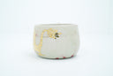 Ceramic cup with a thin handle, off white with subtle red splatter coloring. A gold dragon is painted onto the front of the mug.