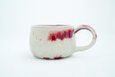 Ceramic cup with a thin handle, off white with subtle red splatter coloring. A gold dragon is painted onto the front of the mug.
