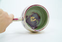 Inside view of the mug, with green coloring and purple splatters and a gold signature.