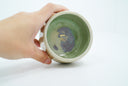 Inside of ceramic bowl, mint green with purple splotches and gold signature of artist.